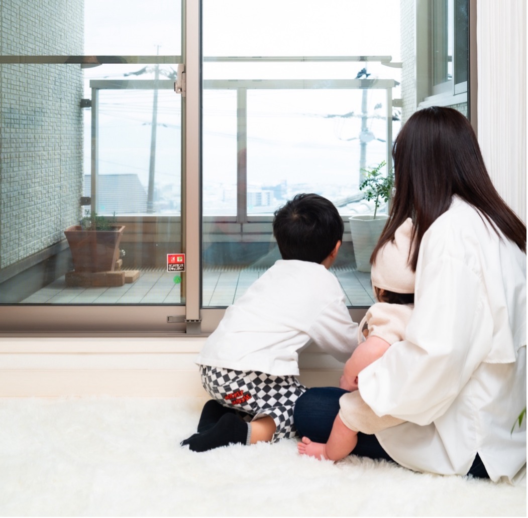 窓際に座る子どもと赤ちゃんを抱く母親｜子育て世帯の窓の暑さ対策